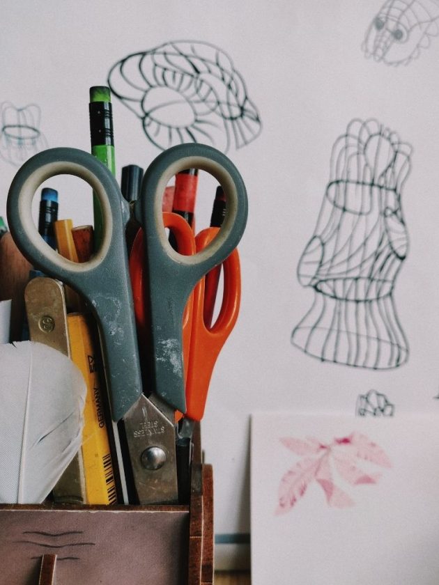 Scissors and pencils in basket with sketches in the background