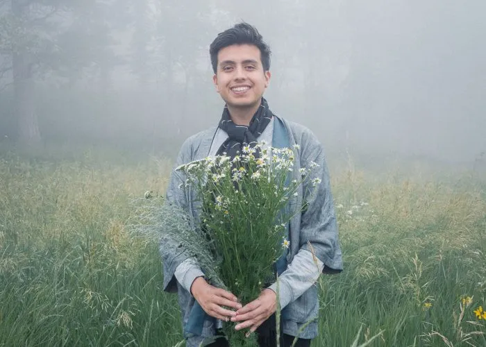 Isaias Hernandez holds a bunch of flowers in a misty field
